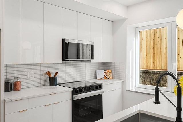 kitchen with decorative backsplash, sink, white cabinetry, light stone countertops, and black range with electric cooktop