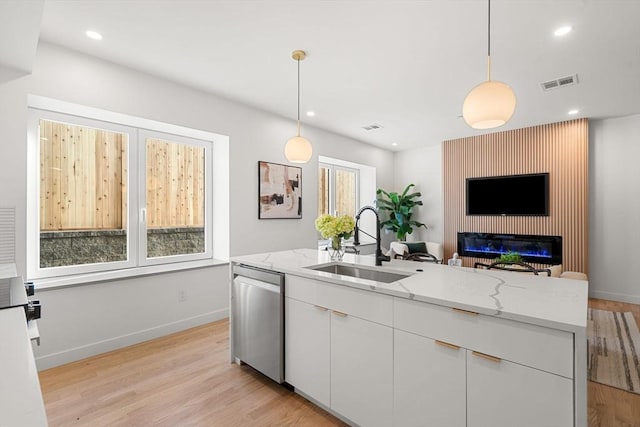 kitchen featuring pendant lighting, stainless steel dishwasher, sink, white cabinetry, and light stone countertops