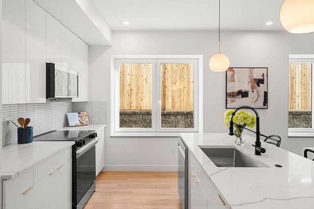 kitchen with electric range, hanging light fixtures, light stone countertops, white cabinets, and sink