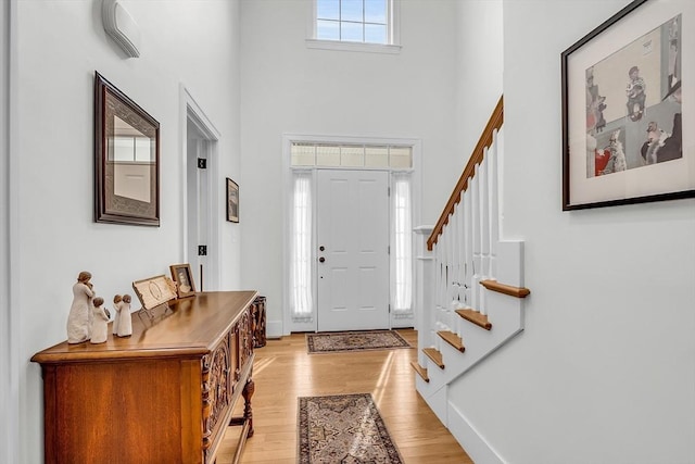 entryway with stairway, a high ceiling, baseboards, and light wood finished floors