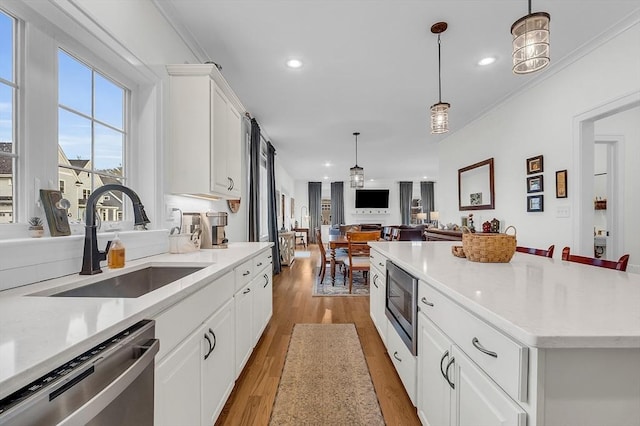 kitchen featuring hanging light fixtures, a sink, light wood-style floors, stainless steel appliances, and white cabinetry