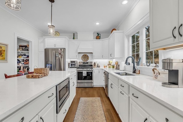 kitchen with crown molding, white cabinets, appliances with stainless steel finishes, a sink, and light countertops