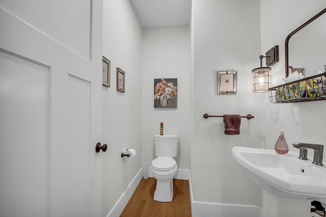 half bath with baseboards, a sink, wood finished floors, and toilet