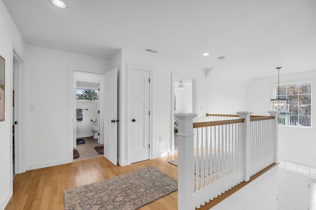 hallway featuring visible vents, a wealth of natural light, an upstairs landing, and light wood-style floors