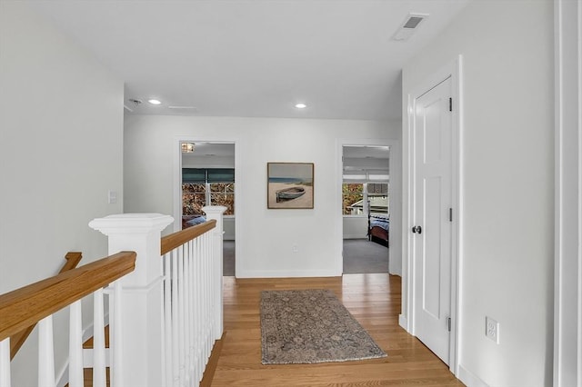 corridor with visible vents, wood finished floors, baseboards, recessed lighting, and an upstairs landing