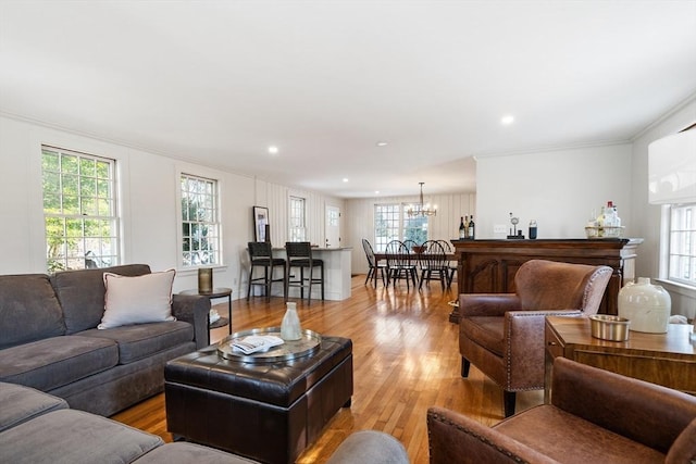 living room with ornamental molding, an inviting chandelier, and light wood-type flooring