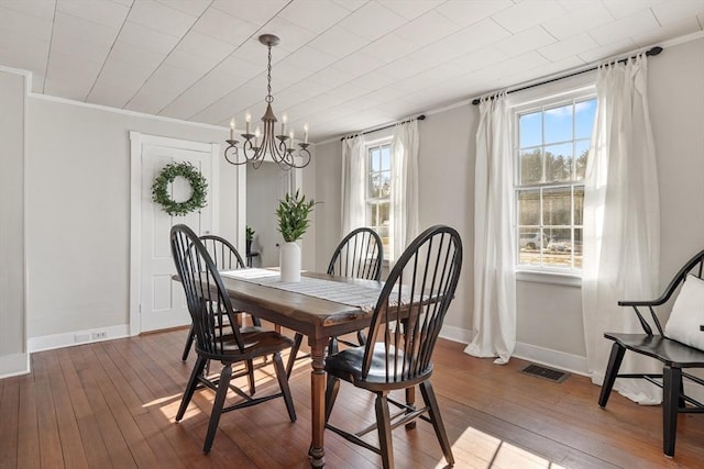 dining area with dark wood-type flooring, crown molding, and a chandelier