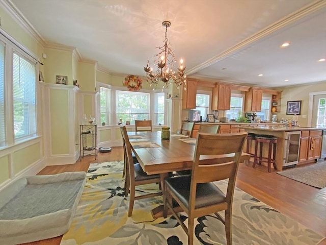 dining room featuring light wood finished floors, wine cooler, a chandelier, crown molding, and recessed lighting