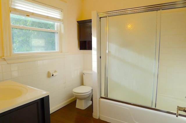 full bath featuring tile walls, wood finished floors, bath / shower combo with glass door, toilet, and vanity