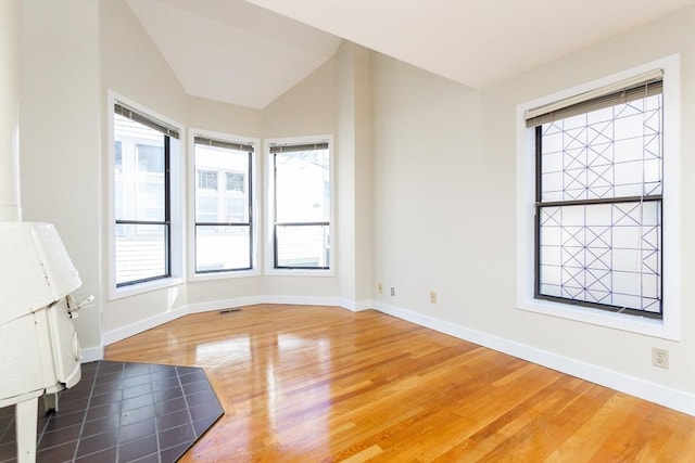 unfurnished room with visible vents, lofted ceiling, baseboards, and wood finished floors