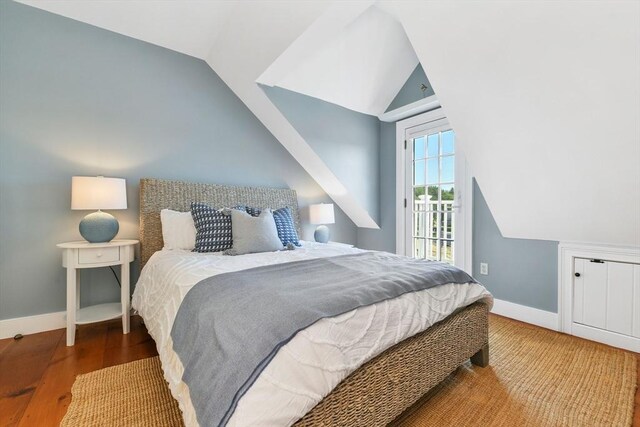 bedroom with lofted ceiling, wood finished floors, baseboards, and access to outside