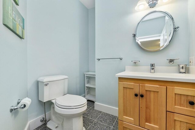 half bath with baseboards, toilet, and vanity