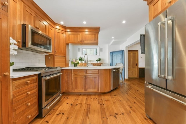 kitchen with appliances with stainless steel finishes, a sink, a peninsula, light wood-style flooring, and light countertops