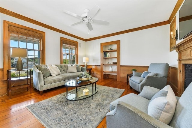 living area featuring healthy amount of natural light, wainscoting, wood-type flooring, ornamental molding, and a fireplace