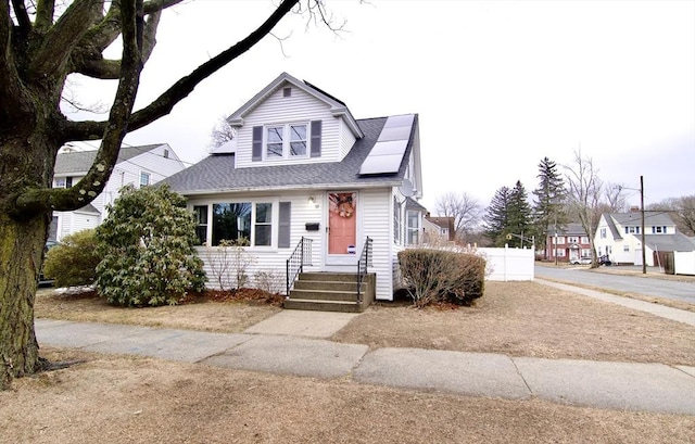 bungalow-style house featuring solar panels, a shingled roof, and fence