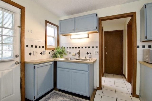 kitchen with light tile patterned floors, light countertops, blue cabinetry, and a sink