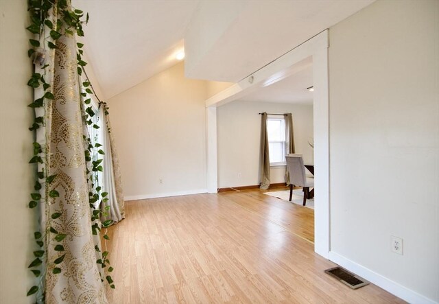 spare room with vaulted ceiling, light wood finished floors, visible vents, and baseboards