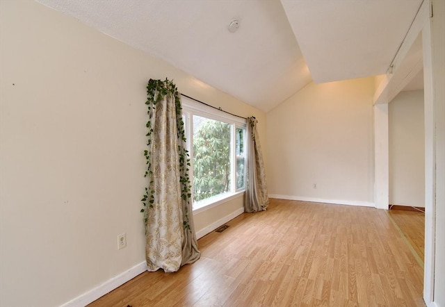 empty room with visible vents, vaulted ceiling, light wood-style flooring, and baseboards