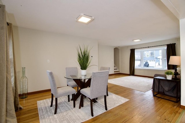 dining space with light wood-style floors, baseboards, and stairs