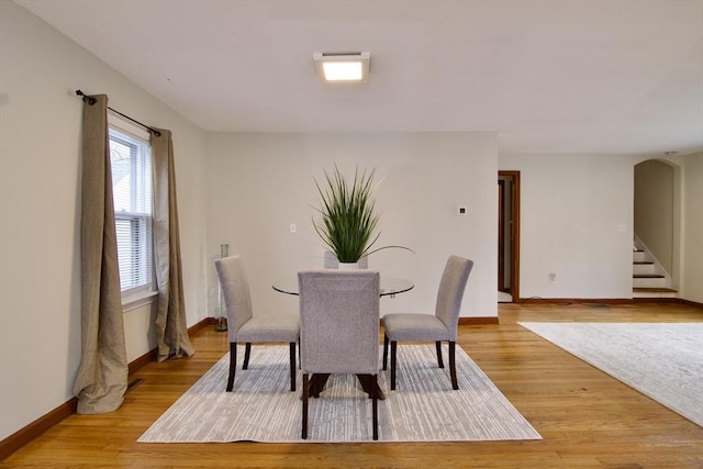 dining room with arched walkways, baseboards, stairs, and light wood-style floors