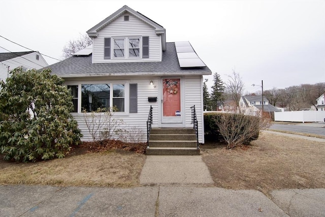 bungalow-style home with fence, solar panels, and roof with shingles