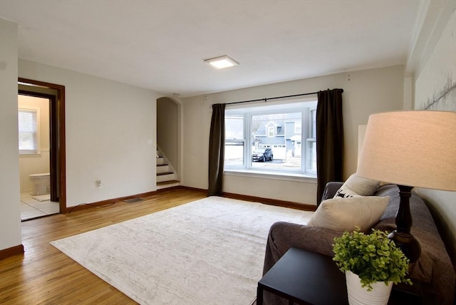 living area with stairs, light wood-type flooring, arched walkways, and baseboards