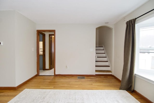 unfurnished room with visible vents, baseboards, arched walkways, stairway, and light wood-style floors