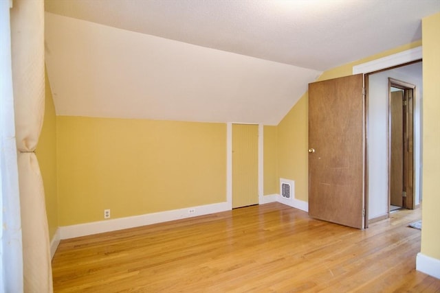 additional living space with lofted ceiling, light wood finished floors, visible vents, and baseboards