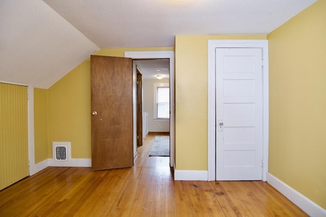 additional living space with lofted ceiling, visible vents, baseboards, and wood finished floors