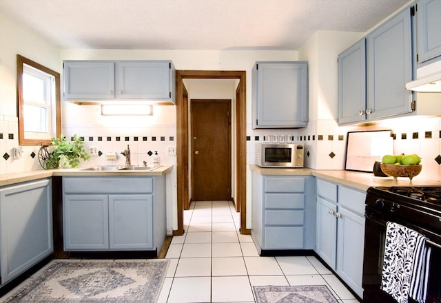 kitchen featuring light tile patterned floors, black gas range oven, light countertops, under cabinet range hood, and a sink