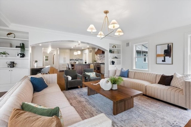 197 Winchester St Unit 197, Brookline, MA 02446 - living room featuring arched walkways, a chandelier, built in shelves, ornamental molding, and light wood-type flooring
