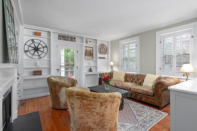 living area with built in shelves, hardwood / wood-style floors, a fireplace with flush hearth, a healthy amount of sunlight, and ornamental molding