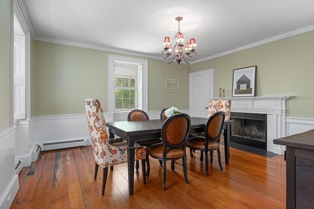 dining area featuring crown molding, an inviting chandelier, wainscoting, baseboard heating, and wood-type flooring
