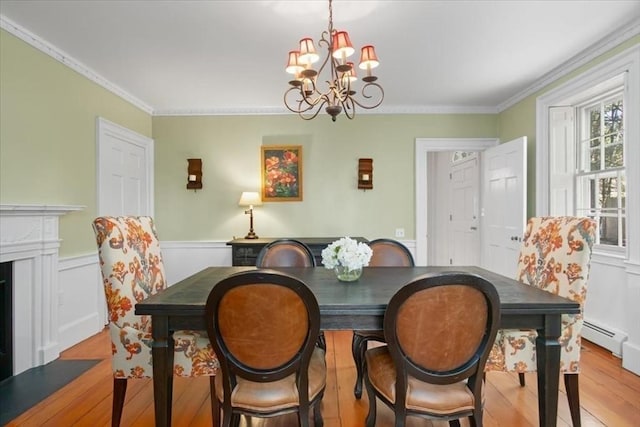 dining area featuring crown molding, wainscoting, a baseboard radiator, an inviting chandelier, and light wood-style flooring