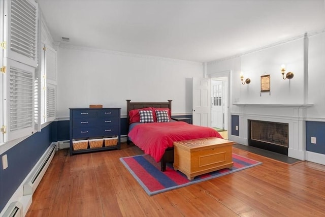 bedroom with visible vents, a fireplace with flush hearth, hardwood / wood-style flooring, a baseboard radiator, and ornamental molding