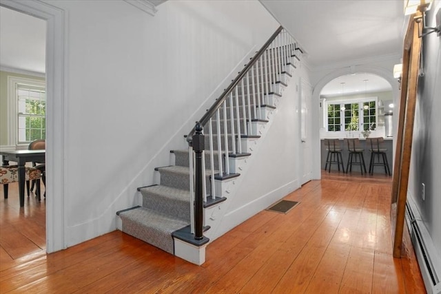 stairs with arched walkways, a baseboard radiator, wood-type flooring, and visible vents