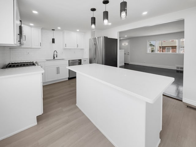 kitchen with hanging light fixtures, a center island, light hardwood / wood-style flooring, appliances with stainless steel finishes, and sink