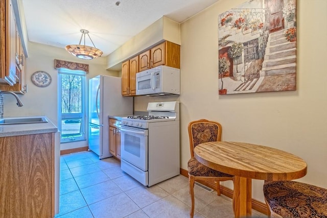 kitchen with white appliances, brown cabinets, light tile patterned floors, and a sink