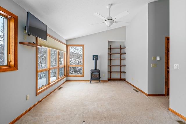 carpeted empty room featuring ceiling fan, vaulted ceiling, and a wood stove