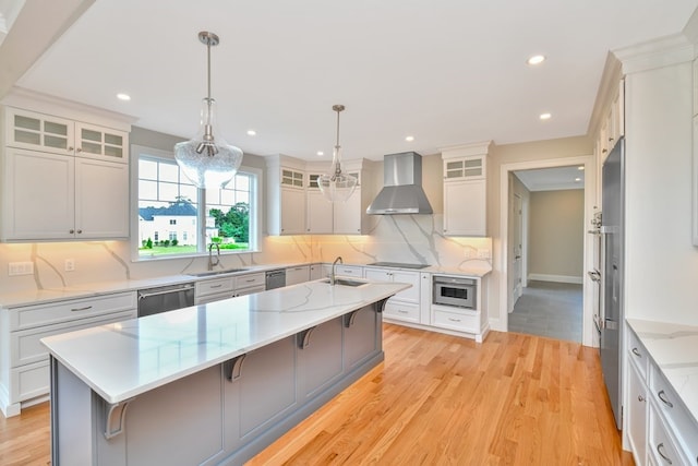 kitchen with light hardwood / wood-style flooring, wall chimney range hood, decorative backsplash, pendant lighting, and a kitchen bar