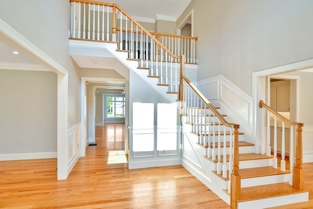 staircase featuring a high ceiling, crown molding, and light hardwood / wood-style floors