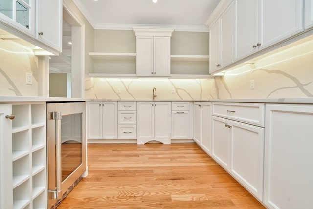 kitchen with crown molding, light wood-type flooring, white cabinets, and light stone countertops