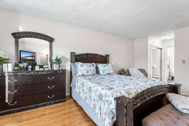 bedroom with connected bathroom, light wood-type flooring, and baseboards