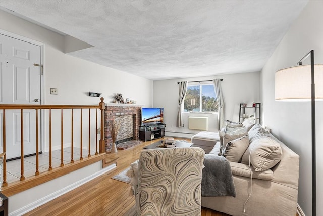 living room featuring a textured ceiling, a baseboard heating unit, baseboards, and wood finished floors