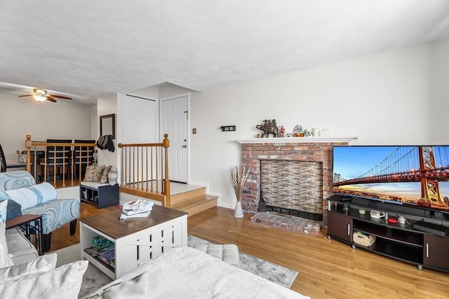 living area featuring a ceiling fan, a brick fireplace, wood finished floors, and baseboards