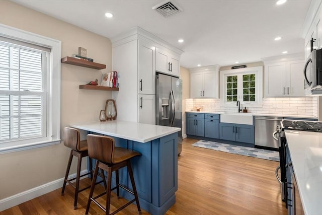kitchen featuring appliances with stainless steel finishes, white cabinetry, light wood-style flooring, tasteful backsplash, and recessed lighting