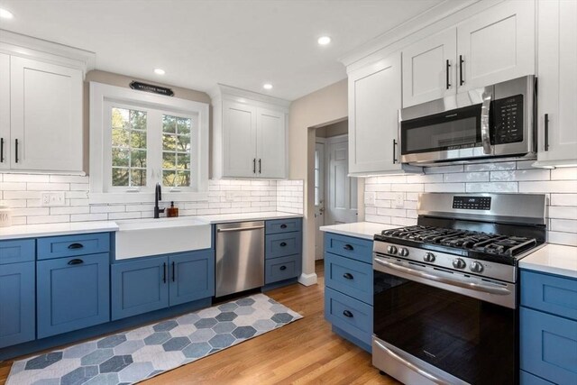 kitchen with stainless steel appliances, a sink, blue cabinets, light wood finished floors, and white cabinetry