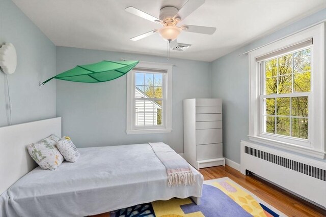 bedroom featuring radiator heating unit, wood finished floors, a ceiling fan, and baseboards