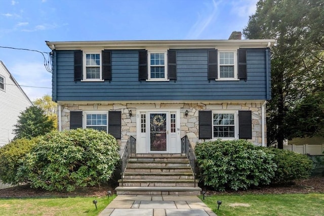 colonial home featuring entry steps, stone siding, and a chimney