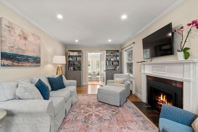 living area with a warm lit fireplace, crown molding, recessed lighting, and wood finished floors